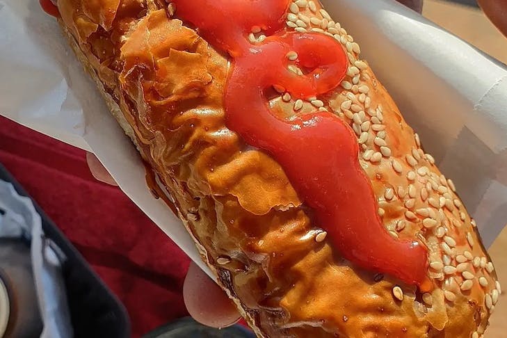 A sausage roll dusted with sesame seeds and covered with tomato sauce